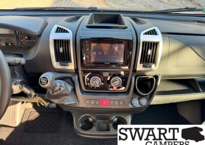 Interior shot of a vehicle dashboard: manual gear shift, keys in ignition, steering wheel to the left, center touchscreen, dual air vents, climate dials, and cupholders.