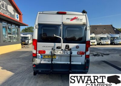 Rear view of a white Fiat Ducato camper with a bike rack, license plate NT-628-G, in a dealership lot with Swart Campers branding nearby.