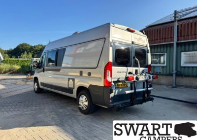 Beige high-roof camper van with a rear-mounted bike rack, parked on a paved lot, SWART CAMPERS watermark in the corner.