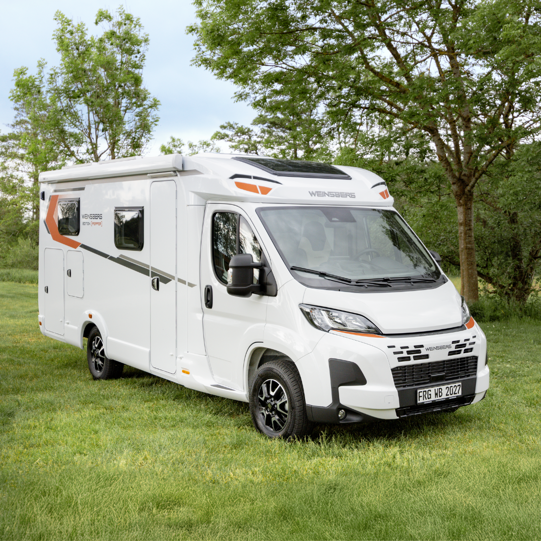 White motorhome parked on a grassy field with trees in the background.