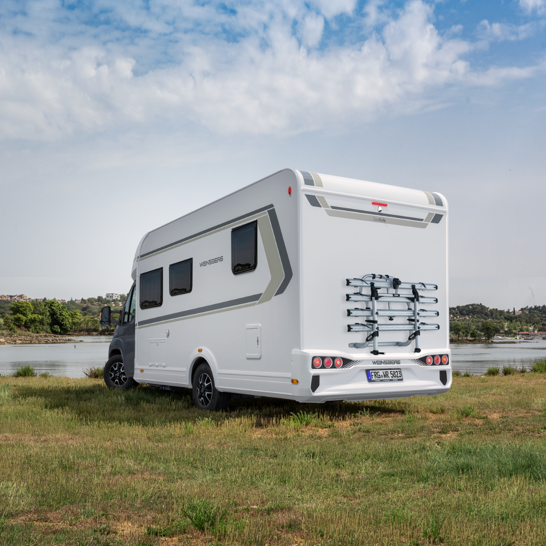 White motorhome parked on grassy field by a lake, with a bike rack on the rear.