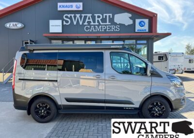 Side view of a gray Westfalia camper van parked in front of Swart Campers showroom with KNAUS signs above the entrance.