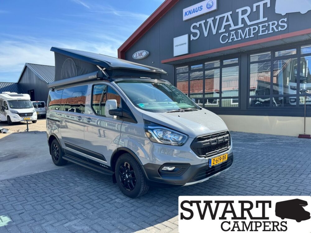 Grey camper van with raised pop-top roof parked outside Swart Campers showroom.