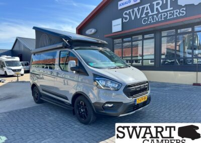 Grey camper van with raised pop-top roof parked outside Swart Campers showroom.