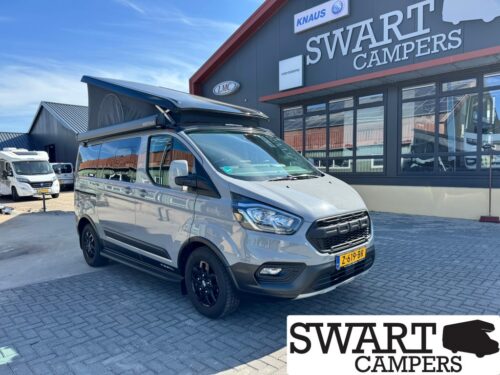 Grey camper van with raised pop-top roof parked outside Swart Campers showroom.