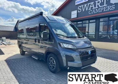 Front three-quarter view of a dark gray camper van with a high roof parked outside a Swart Campers storefront with a bold sign above the windows.