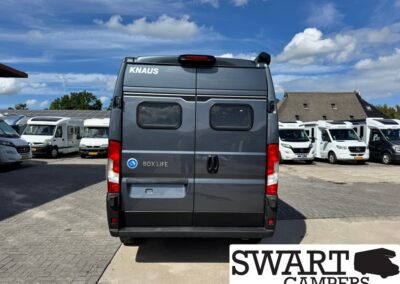 Rear view of a dark gray Knaus Box Life camper van in a dealership lot with white motorhomes in the background.