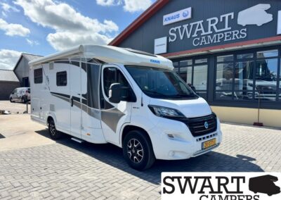 White motorhome with gray/black graphics parked outside Swart Campers showroom under a blue sky.