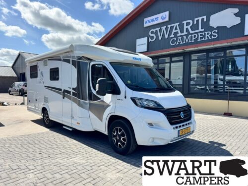 White motorhome with gray/black graphics parked outside Swart Campers showroom under a blue sky.