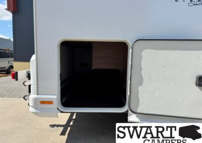 Open side storage compartment of a white camper van, showing a dark interior and wood cabinet inside; logo watermark reads SWART CAMPERS at bottom right.