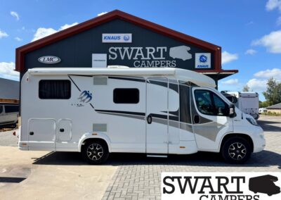 White motorhome parked in front of a Swart Campers dealership building with a large sign and blue sky above.