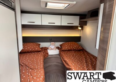 Twin camper beds with brown polka dot bedding, a teddy bear between pillows, and warm overhead lighting from cabinets above.