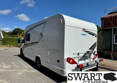 White Knaus motorhome seen from rear-left outdoors on a sunny day, bike rack mounted on back.