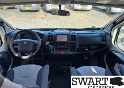Interior view of a camper van cab with steering wheel, manual gear stick, center touchscreen, and two front seats; SWART CAMPERS logo in the bottom right corner.