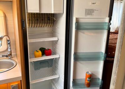 Open camper fridge with peppers on a middle shelf and a blue bin; the opposite door has three clear shelves, one with a can of Fanta on the bottom shelf.