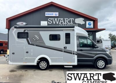 Side view of a silver and dark gray motorhome parked in front of a Swart Campers showroom with assorted logos on the facade (Knaus, LMC).