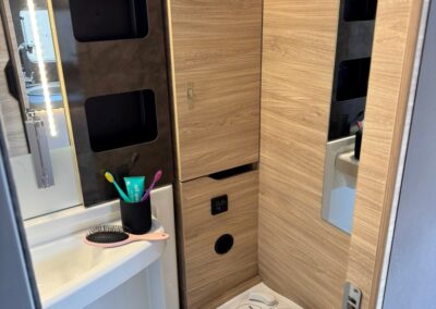 Compact camper bathroom with wood panel walls, a small sink, toothbrush holder, hairbrush, and a compact toilet with built‑in controls.