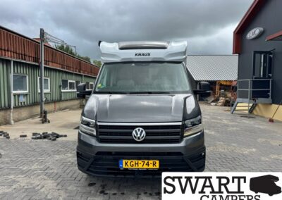 Front view of a gray VW camper van with a raised KNAUS roof, parked in a paved industrial yard, Swart Campers watermark visible.