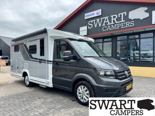 KNAUS VAN TI VW 640 MEG VANSATION - Swart Campers Front three-quarter view of a white and gray motorhome parked outside a camper dealership. Large 'SWART CAMPERS' sign is visible on the building.
