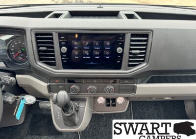 Interior car dashboard with central touchscreen, climate controls, and gear shifter; keys in ignition and a 'SWART CAMPERS' logo in the corner.