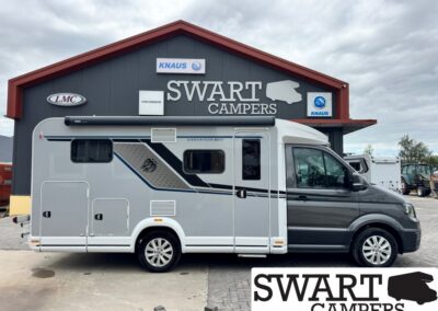 Grey and white camper van parked in front of a Swart Campers building with logos visible on the facade.