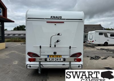 Rear of a white Knaus caravan with a bike rack attached to the bumper and license plate KJR-24-R, on a cloudy day.
