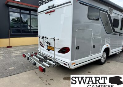 Rear view of a white Knaus camper van with a mounted bike rack and Dutch license plate KJR-24-P, parked outside a building.
