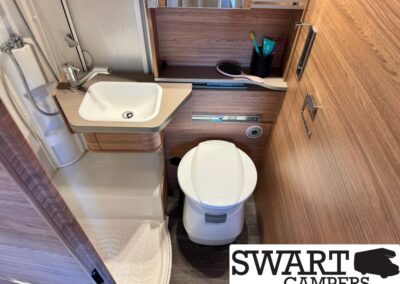Compact camper bathroom with small sink, toilet, and shower enclosure in wood-paneled interior