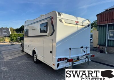 Rear view of a white motorhome parked on a brick lot, featuring a bike rack at the back and visible taillights/registration plate area.