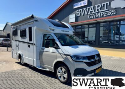 White camper van with 'WENNSBERG' branding parked in front of a Swart Campers showroom sign on a sunny day.