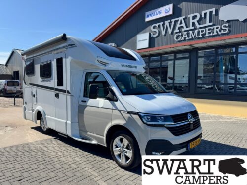 White camper van with 'WENNSBERG' branding parked in front of a Swart Campers showroom sign on a sunny day.