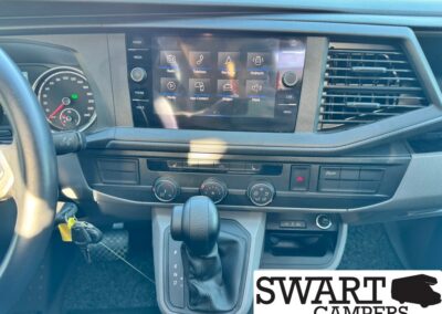 Dashboard view of a vehicle interior with a center touchscreen showing apps, and a gear shifter in the foreground.