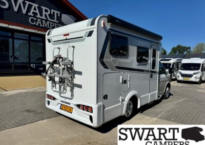 Rear view of a white camper van with a mounted bike rack, parked in front of a dealership.