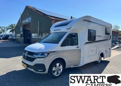 White Weinsberg motorhome parked outside a workshop with green corrugated metal walls and a blue sky. Swart Campers branding visible in the foreground right.