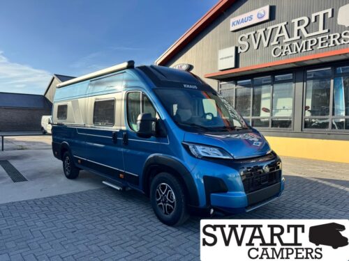 Blue camper van with a raised roof parked at a Swart Campers showroom, with the dealership name visible on the building behind it.