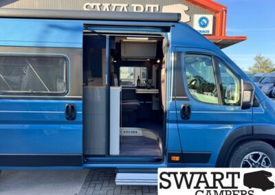 Blue camper van with the side door open, revealing a compact kitchenette and seating area inside. The Swart Campers logo is visible in the bottom-right corner.