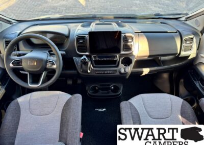 Interior of a Fiat camper van cockpit with steering wheel, central touchscreen, and two front seats