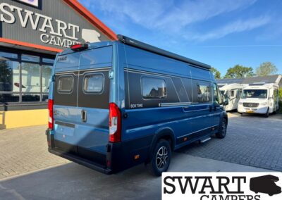 Blue KNAUS BoxTime camper van parked outside a Swart Campers dealership with an extended awning and other RVs in the lot.
