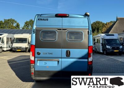 Rear view of a blue Knaus camper van with two small rear windows, parked among other motorhomes.
