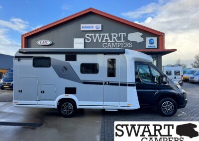 White and gray motorhome parked in front of a Swart Campers building with red roof and logos, side doors and windows visible.