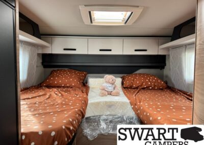 Twin camper beds with orange polka-dot bedding and a stuffed bear between them in a compact bedroom area.
