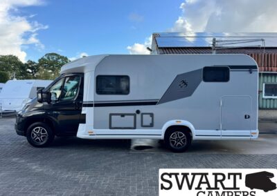 White/gray motorhome parked on a paved lot, solar panels on its roof and a side window visible, with other caravans in the background.