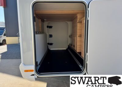 Open rear storage area of a campervan showing a black floor, light wood cabinets on the right, and a small door at the far end