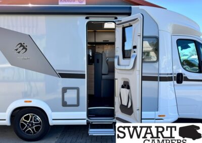 Exterior view of a white motorhome with its side door open, showing the step and interior seating area inside the living space. Brand decal and a SWART CAMPERS watermark are visible on the lower right.