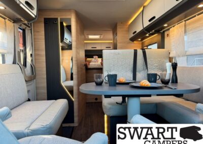 Interior of a modern campervan with a dining table set for two to four, croissants and mugs on plates, and warm wood accents.
