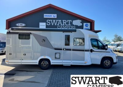White motorhome parked in front of a Swart Campers dealership building under a blue sky.