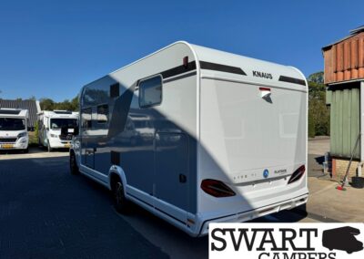 Rear three-quarter view of a white KNAUS motorhome caravan parked on a paved lot with other campers nearby on a sunny day.