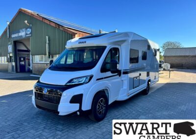 White Knaus camper van parked outside a workshop with a 'Garage Swart' sign under a blue sky.