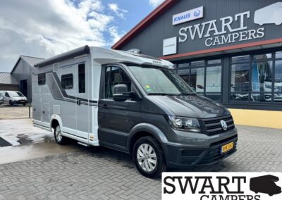Grey and white Volkswagen camper van parked outside the Swart Campers showroom, with the building sign visible.