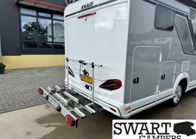 Rear view of a white/gray Knaus motorhome with a bike rack attached to the rear, parked outside a dealership.